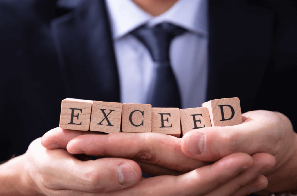 Man in suit arranging wood blocks spelling "EXCEED"