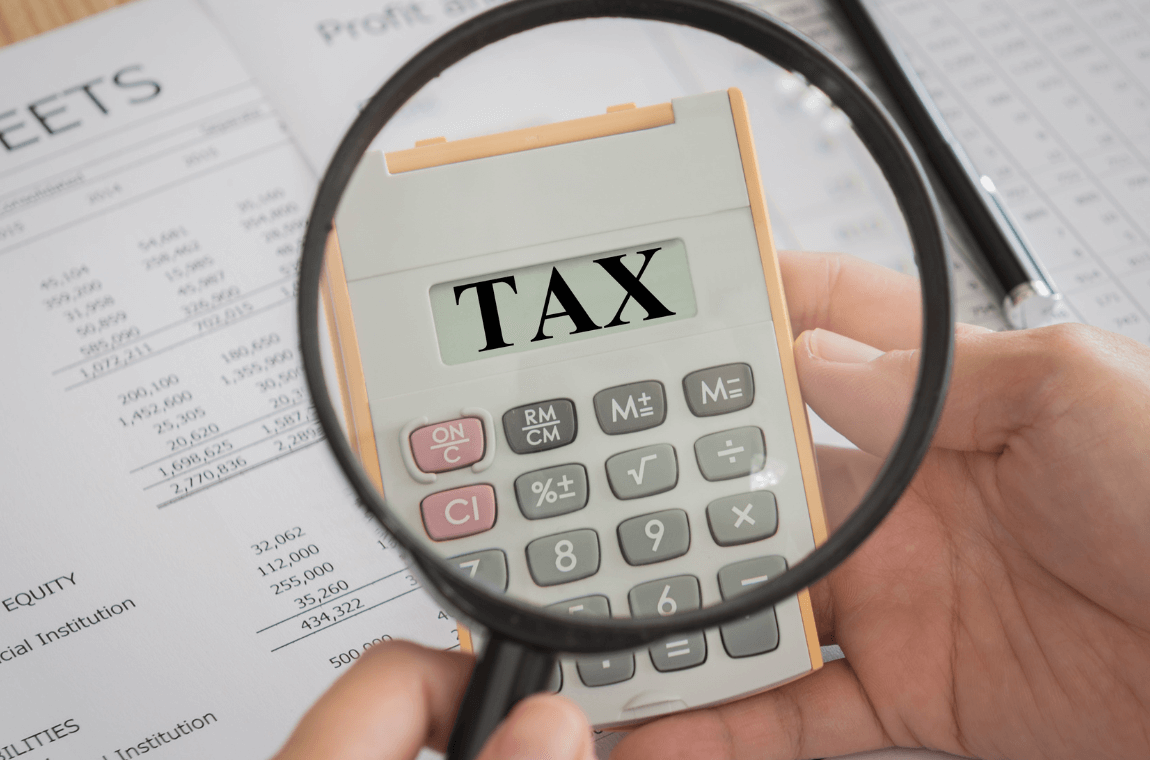 Person examining the word TAX with a magnifying glass amid logistics documents